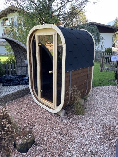 Kleine, moderne Holzhütte mit runder Form und einer Glastür im Garten.
